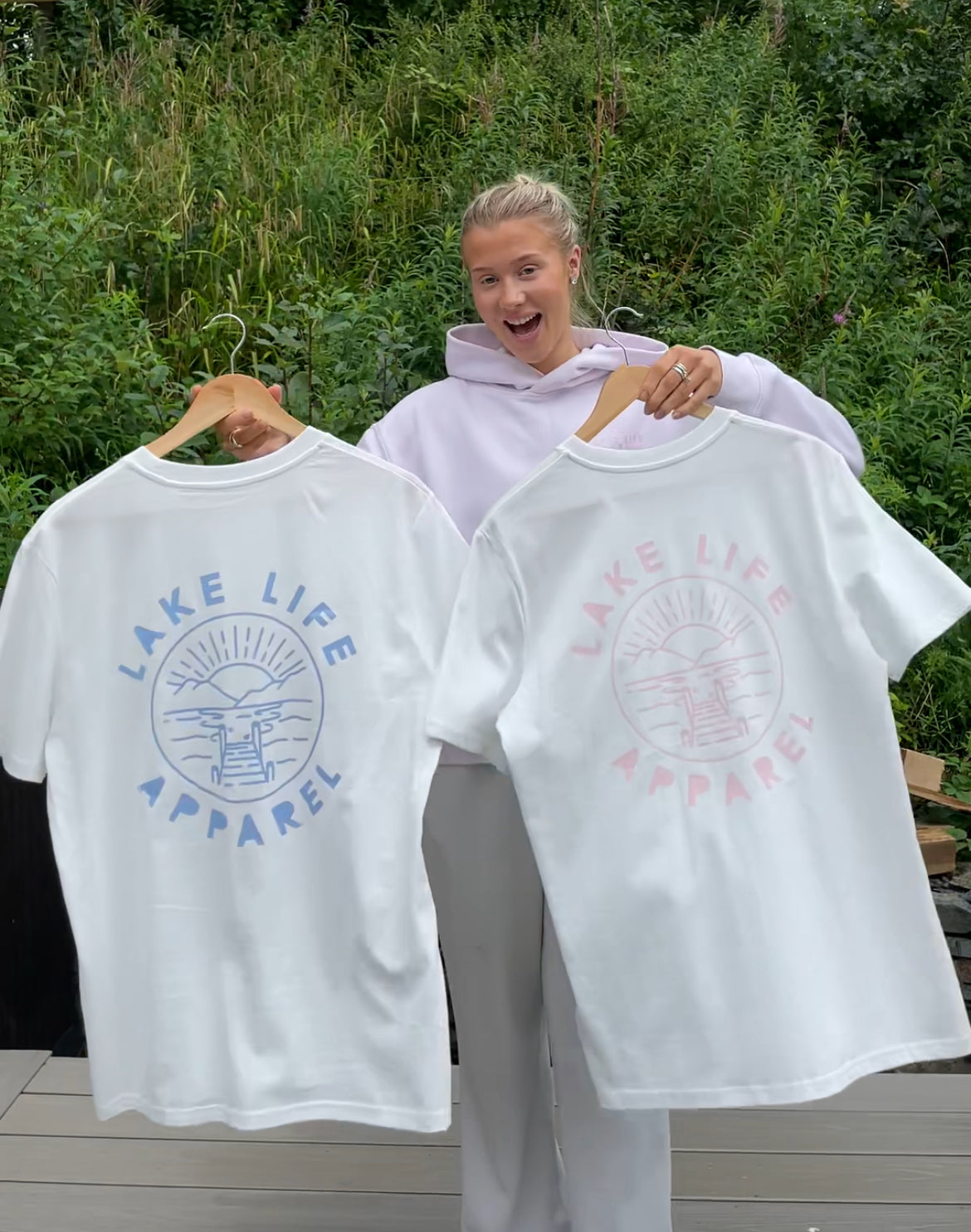 Person holding two 'Lake Life Apparel' t-shirts with branding outdoors.