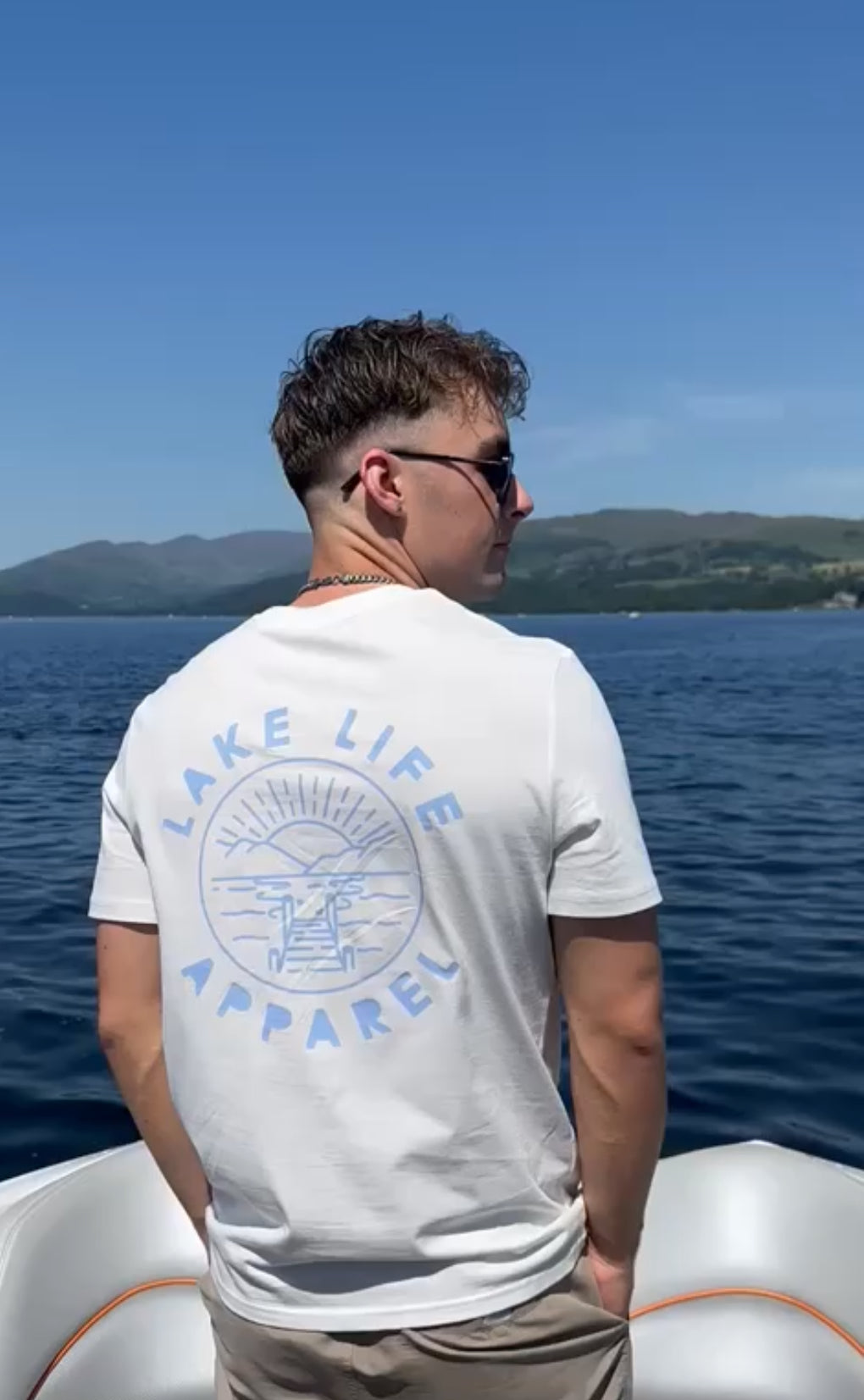 Person wearing a 'Lake Life Apparel' t-shirt on a boat with a scenic background